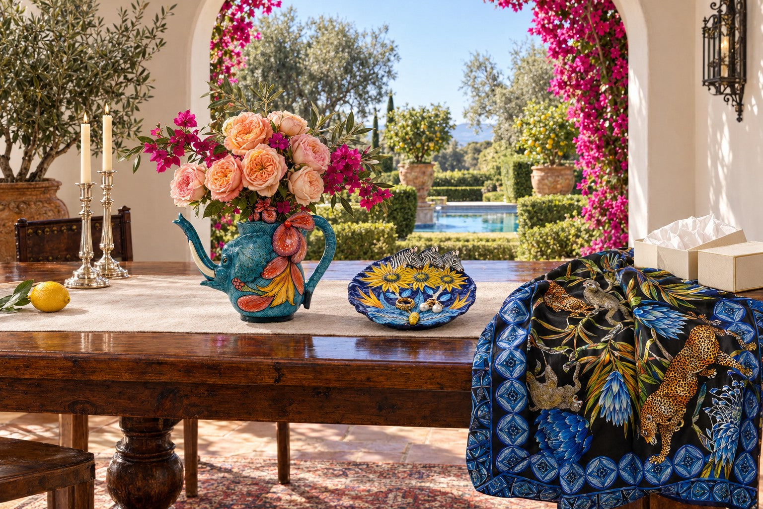 An elephant teapot full of roses and bougainvillea, a zebra coin dish and a silk scarf on a walnut table in a sunlit Montecito loggia