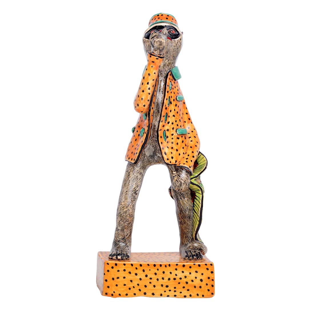 A monkey wearing orange coat & hat showing his thumbs up sculpture